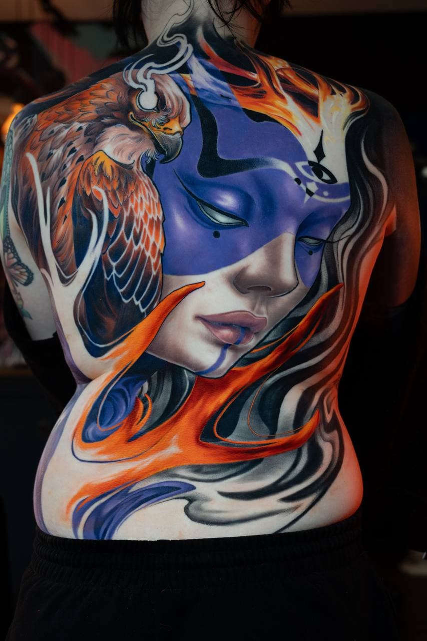 Full back tattoo by veda.ink: a woman's face in purple with an eagle and orange flames, colour illustration style