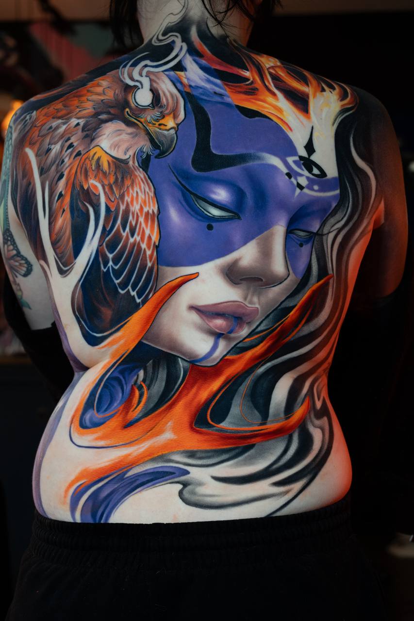 Full back tattoo by veda.ink: a woman's face in purple with an eagle and orange flames, colour illustration style